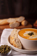 warm autumnal setting with creamy pumpkin soup, artisan bread, and toasted pumpkin seeds on a rustic wooden table, prepared, elegant, appetite, savory, wholesome, simple, hearty, nutritious, organic