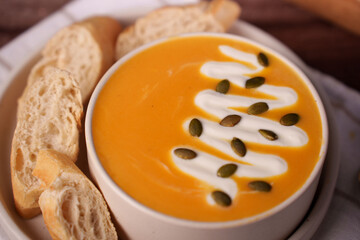 creamy pumpkin soup with whipped cream and pumpkin seeds in white bowl with slices of crisp baguette on the side creating a warm and inviting culinary presentation, nutty, wholesome, satisfying