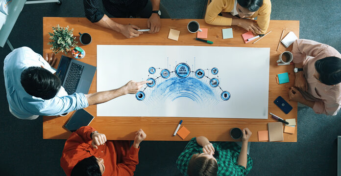 A diverse team engages in a collaborative business meeting, illustrating innovative ideas on a mind map. The vibrant workspace includes laptops, documents, and coffee. Trope - Powered by Adobe