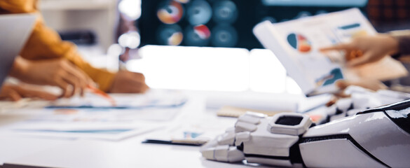 A dynamic business meeting with a diverse team analyzing various data and graphics. Advanced technology and robotics foster collaboration and drive innovative insights.Noogenesis