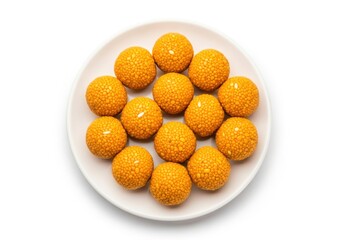 An overhead shot of a white plate piled high with til laddu, a popular indian sweet, isolated on white background