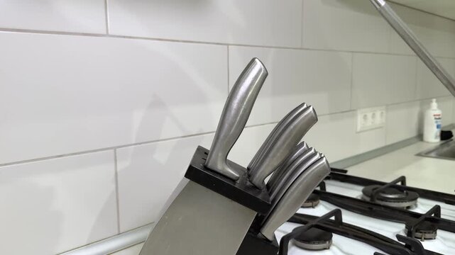 A person sharpening knives between each other. A man takes a knife sharpener out of a knife stand in the kitchen