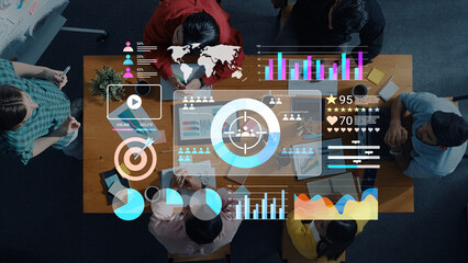 A team of professionals collaborates around a table, engaged in a business analysis meeting featuring digital data visualization and graphs to enhance decision-making. Gantry