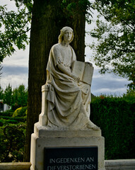 sitzende Frau auf einem Gedenkstein mit einem Buch in der Hand  Friedhof in Goch