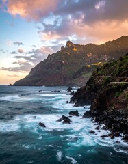 Dramatic coastal view with turbulent water meeting rocky shores and lush green mountains under a sunset sky
