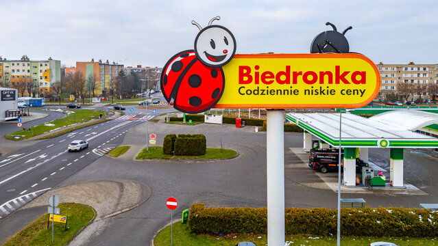 Large Biedronka sign beside BP station surrounded by street traffic, residential buildings and subtle winter conditions across the urban junction area