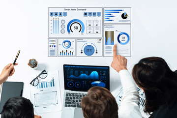 A diverse team in an office setting examines a smart home dashboard on a laptop, discussing key...