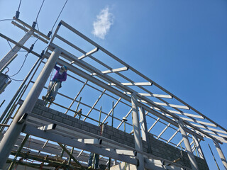 Focused construction worker building steel frame structure on roof under clear blue sky. An industrial scene showing diligent labor, architecture, and engineering