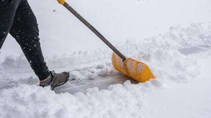 Snow cleaning service worker using a yellow shovel to clear snow from a walkway during a winter storm, showcasing effective snow removal techniques © JuliaDorian