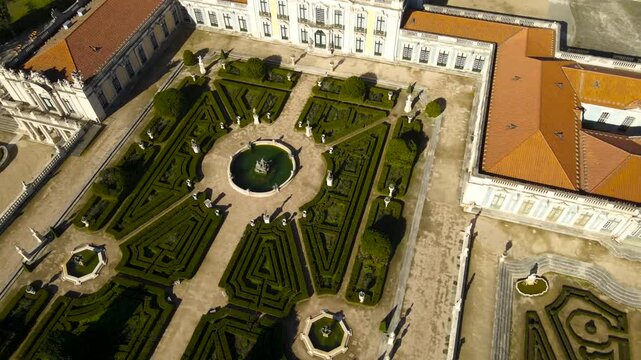 Aerial drone video of the magnificent and royal Queluz palace in Portugal Sintra Lisbon area with large French garden that has fountains and monument white statues in between the plants and trees.