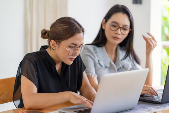 Two Asian Women Working Together in a Bright Minimalist Workspace - Powered by Adobe