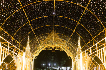 Magical golden light tunnel decoration for festive outdoor festival at night. This glowing arch structure creates an enchanting and celebratory atmosphere for holiday