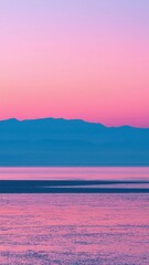 Calm sea with reflections of pink and purple sky during sunset with silhouette of distant mountains