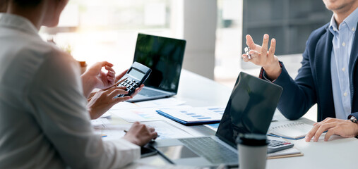 Professional business people discussing finances and calculations in a modern office setting, representing teamwork, planning, and financial analysis.