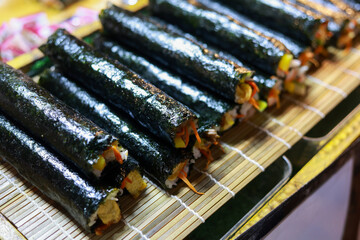 Delicious fresh Korean kimbap rolls on display. Traditional gimbap food made with seaweed and rice, creating an appetizing snack or meal on bamboo mat for takeout