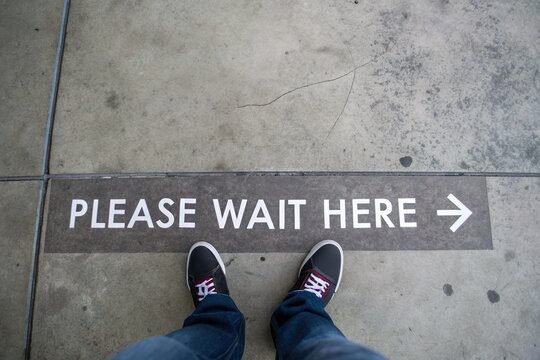 person stand at please wait here floor marker. Waiting queue line