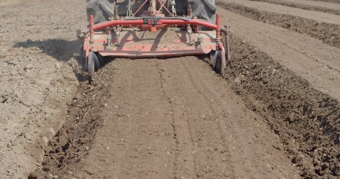 A tractor operates a rotary tiller to create planting rows in farmland, preparing soil structure for vegetable cultivation.