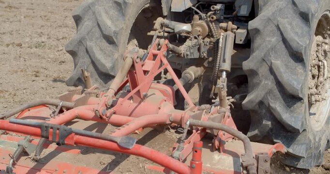 Rotary tiller blades spin through the soil, powered by a tractor engine to break and loosen earth efficiently.