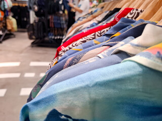 Selective focus on colorful summer Hawaiian shirts hanging on clothing rack in trendy boutique retail store showcasing various tropical prints and vibrant apparel patterns © Rungphailin