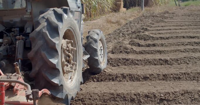 A tractor operates a rotary tiller to create planting rows in farmland, preparing soil structure for vegetable cultivation.