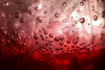 Macro closeup of refreshing red drink with ice and bubbles. carbonated soda beverage and fizzy liquid texture create an intense, moody background for any project