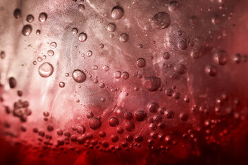Refreshing closeup of cold red beverage with an ice cube and carbonated bubble. macro view of fizzing liquid shows an abstract texture for summer background