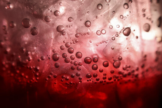 Macro closeup of refreshing red drink with ice and bubbles. carbonated soda beverage and fizzy liquid texture create an intense, moody background for any project