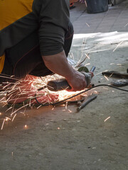 Obraz premium Focused industrial worker cutting metal with grinder, creating bright sparks. Manual labor with man hand using power tool in workshop for construction work