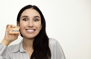 Woman holds whitening trays and hydrogen peroxide syringes, smiling while showing a dental model. White backdrop, close frames with trays, gel and tooth care tools for a bright healthy smile.