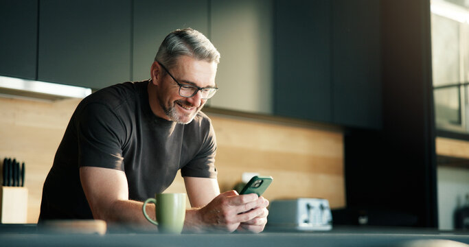 Happy man, scroll and typing in kitchen with phone, social media notification and text message update. Mature person, smile and browsing with tech in home for news feed, online communication or chat. - Powered by Adobe