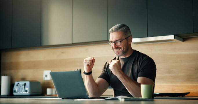 Mature man, fist pump and laptop at house with good news, financial freedom and lotto winner. Excited, male person and cheering with pc for giveaway announcement, finance achievement and celebration