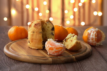 Christmas bread with tangerines on wooden plate with Christmas lights in background
