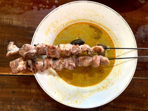 indonesian sate klatak served with curry soup on a white plate and wooden table