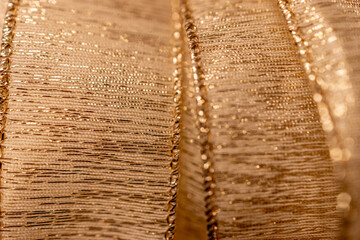 Full frame defocused macro texture background of gold metallic holiday ribbon with glittering strands and bokeh