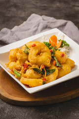 Golden crispy fried prawns with curry leaves and chili served on a white plate on a wooden board.