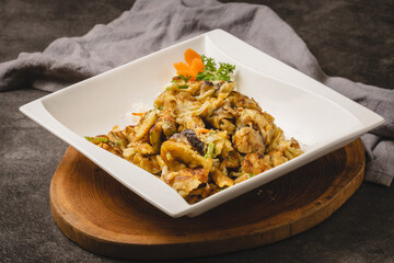 A close-up shot of a delicious stir-fried dish, possibly with eggplant and other vegetables, served in a white square bowl on a wooden board.