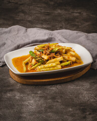 A vibrant stir-fried dish with green vegetables and meat in a rich orange-red sauce, served on a white plate.