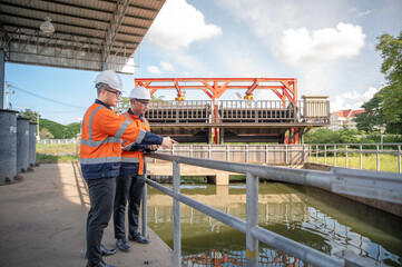 Industrial engineering team evaluating equipment conditions and discussing project tasks near the water gate