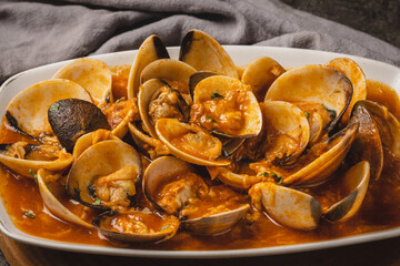 A close-up shot of a delicious plate of steamed clams in a rich, reddish-orange sauce, garnished with fresh green herbs, ready to be served.