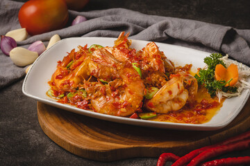 Delicious Indonesian-style spicy prawns with petai beans and chili sauce served on a white plate with fresh ingredients in the background.