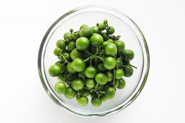 Top view of fresh ranti (leunca), displayed in a clear glass bowl and isolated on a clean white background.