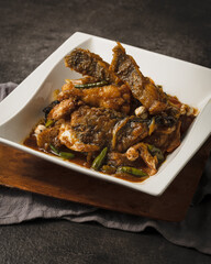 Close-up of a delicious fish curry or stew with green chilies served in a white bowl on a wooden board.