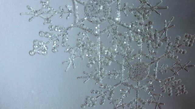 Glittering clear plastic snowflake ornament swaying gently, set against a textured gray background