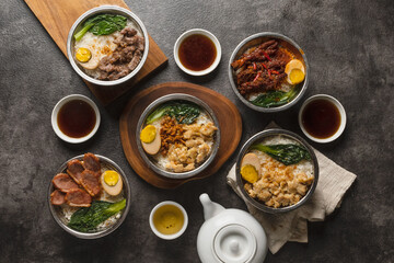 A top-down view of several Asian rice bowls, including braised pork and other meat dishes, served with tea and sauces on a dark, textured surface.
