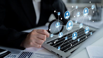 A business professional uses a magnifying glass to analyze digital network connections on a laptop, highlighting the integration of technology in today workplace. Tessel