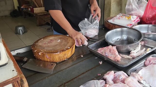 Vendor packing freshly cut chicken parts into plastic bags. Fresh chicken wings being packed by a vendor at the market. Butcher packs cut chicken parts into bags for customers