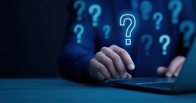 Question mark graphic over person using laptop computer for online support and problem solving in dark blue tones conceptual image
