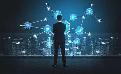A businessman stands in front of a digital interface, visualizing data connections and infographics in a modern urban environment. The blue light adds a futuristic touch. Tessel