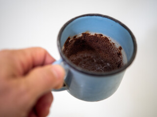 Hand holding an old rusty enamel mug with heavy rust buildup inside. Close-up of worn, damaged metal cup with corroded interior.