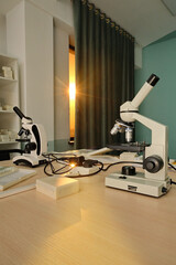 Educational lab with compound microscopes, slides, and documents on a sunlit wooden table near a window.